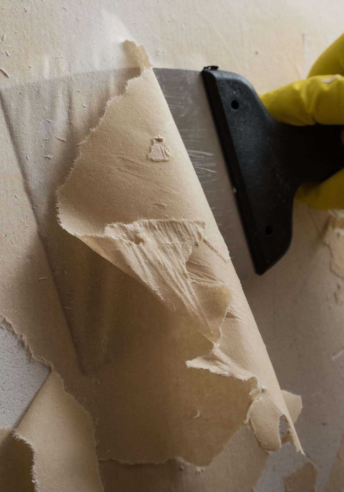 Preparing the wall for painting or sticking new wallpaper. Man in yellow gloves with a scraper in the process of removing old wallpaper. wetted with a special solution surface